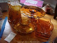Overview of amber colored glassware including pitcher, cake plate on pedestal, bowls, and rectangular dishes.