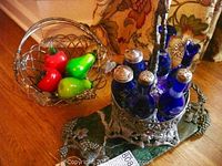 Full view of the cruet set with cobalt blue crystal bottles in pewter holder and wire basket with glass fruit
