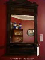 Full view of antique wood-framed mirror mounted on a red wall, showing the mirror reflection and frame details.