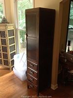 Side view of tall wooden cabinet showing four drawers below and closed door above