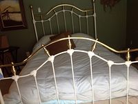 Full view of assembled brass and white metal bed frame with bedding on a mattress.