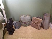 Photo shows three stone-like decorative signs: a heart-shaped one with floral border and inscription, a bird sign, and a square floral relief plaque, alongside two translucent screen cylinders or lanterns.
