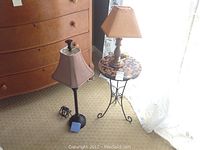 Photo showing both lamps and the metal table with mosaic top next to a wooden dresser and near a sheer curtain, providing overall lot view.