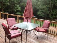 Overall view of square outdoor table with umbrella and four chairs with burgundy cushions on deck.
