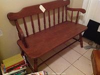 Full view of the wooden bench showing spindle back, armrests, and seat surface.