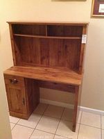 Front view of wood desk with hutch showing three open shelves in hutch, rectangular desk surface, cabinet door, and drawer on left side
