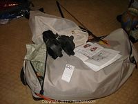 Tan camping tent in carry bag with poles and manual, youth black bow with arrows visible