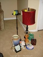 Photo showing the tall table lamp with red fabric shade, candle holder, and cluster of vases, frames, coasters, and night light on carpeted floor.