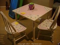 Photo showing the children's square table with pink floral top and two matching chairs around it, placed on carpet; condition shows some light wear.