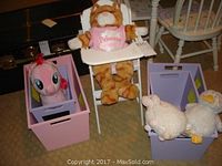 Full view of four storage containers with plush toys including large giraffe, My Little Pony, and two sheep plushies on and next to containers, with white metal doll high chair behind giraffe plush.
