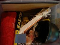 Toys including Easton baseball bat, black and green helmet, red fabric bag, and a globe inside a plastic bin