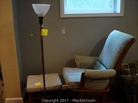 Glider rocker chair with light blue upholstery, matching ottoman, and antique brass floor lamp in room corner under window