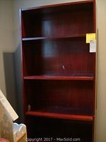 Tall reddish-brown wooden bookcase with five shelves shown from the front against a neutral wall.