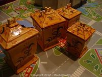 Set of four yellow-orange ceramic canisters shown together on a colorful mat, all square-based with decorative lids.