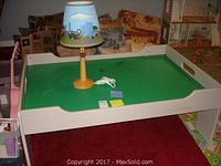 Children's wooden game table with green top and white frame, showing surface scratches, placed indoors on carpet.