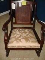 Front view of antique wood rocking chair showing cane backrest and upholstered floral seat.