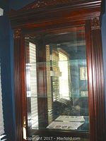 Front view showing ornate carved top and glass door with visible adjustable shelves inside.