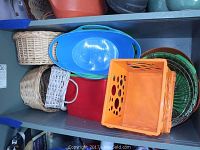 Top-down view showing the assortment of baskets stacked together including wicker baskets, colored plastic trays, orange plastic crate basket, and metal wire baskets.