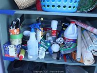 Shelf with assorted household products including tapes, cleaners, spray bottle, contact paper, and paint brushes.