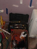 Tool box with hand tools and extension cords around it in a room corner