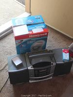 Photo showing Honeywell Compact Air Purifier in its original red and blue box with white air purifier unit and accessories box displayed on top, placed on floor indoors.