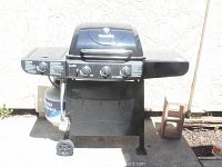 Full view of Char-Broil gas grill including side burner, propane tank underneath, and cleaning brush hanging on front.
