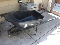 Side view of black metal UnionTools wheelbarrow with wood handles, showing wheelbarrow basin, handles, and tire.