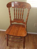 Front view of one wood dining chair showing carved backrest with floral design, turned spindles and solid seat with scratches.