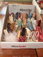 Photo showing a variety of 20 miniature shoe figurines in multiple colors and styles arranged in a MaxSold box. Some shoes have decorative details such as feathers, bows, glitter, and flowers.