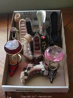 Photo showing seven miniature shoe figurines placed inside a cardboard box, varied styles, some with large gem details on the toe, including leopard print and metallic silver styles