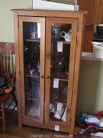 Front view of wood cabinet with closed glass panel doors showing four internal shelves with some items inside.
