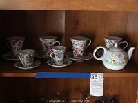 Photo of six floral tea cups and saucers plus two smaller cups and saucers and the Westwood teapot on a wood shelf.