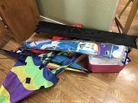 Lot of various kites and mini Rubbermaid cooler on wooden floor next to furniture