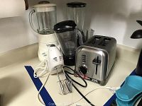 Countertop with small appliances including Cuisinart blender, Hamilton Beach blender, Durabrand hand mixer, and Cuisinart toaster showing layout and cords.