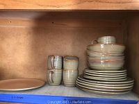 Photo of stacked dishes including plates, bowls and mugs showing overall condition and style.