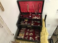 Overall view of black jewelry box open showing red velvet lining and multiple compartments filled with jewelry