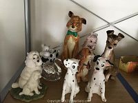 Full view of assorted Disney dog figurines on shelf including Dalmatians, brown dog in green bow tie, pink poodle, white poodles, and a glass swan.