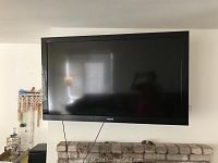 Front view of the Sony Bravia TV mounted on a wall above a fireplace. TV is unpowered and turned off with a black screen.