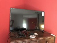 Sharp Roku TV 43-inch screen with cables and remote control on wooden surface against red wall