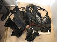 All leather clothing items and gloves laid on the floor, showing two zip-front halter tops including one with butterfly design, leather vest and gloves.