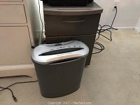 Gray Identity Guard paper shredder positioned next to the filing cabinet, showing the shredder top and side details.