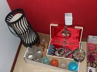 Jewelry box on table with assorted costume jewelry inside, black and white striped candle holder with candle, and multiple colored glass candles in tray.
