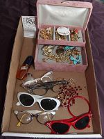 Full view of jewelry box with assorted costume jewelry and eyeglasses in brown cardboard box.