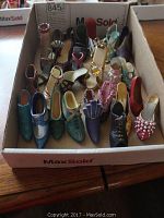 Photo showing a box with more than 15 miniature collectible shoes of various styles and colors including blue, green, purple, and red shoes with different textures and embellishments.