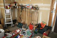Wide view of the lot showing toolboxes on the floor, hand tools, and gardening tools leaning against the wall in a garage space.