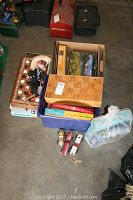 Photo showing a box filled with board games including chess, checkers, Monopoly, Yahtzee, puzzles, and a Mexican made marionette box.