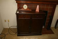 Full view of the dark wood entertainment center with two small drawers and cabinet doors placed against a fireplace wall.