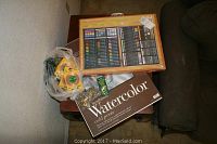 Photo showing the Gallery Masterpiece 147-piece art set in wooden frame, Strathmore watercolor sketch pad, and other accessories grouped together on a table.