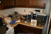 Wide view of corner countertop showing thermoses, coolers, Ball mason jars, crock, and various kitchen items.