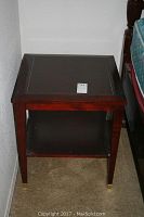 Square wooden table with an open shelf at the bottom placed next to the Thomasville nightstand